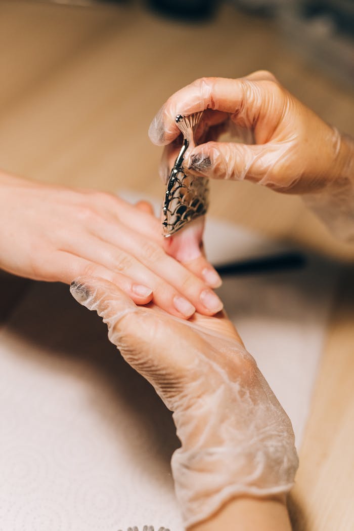 Close-up of a professional manicure showing a nail artist applying intricate nail art with gloved hands.