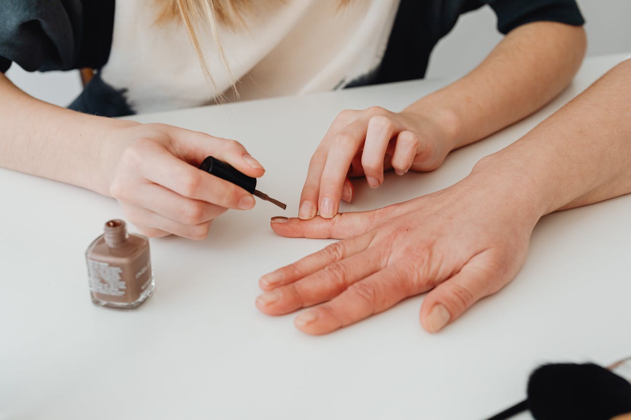 our-services-03 Close-up of hands during a manicure session, applying nail polish in a salon setting.
