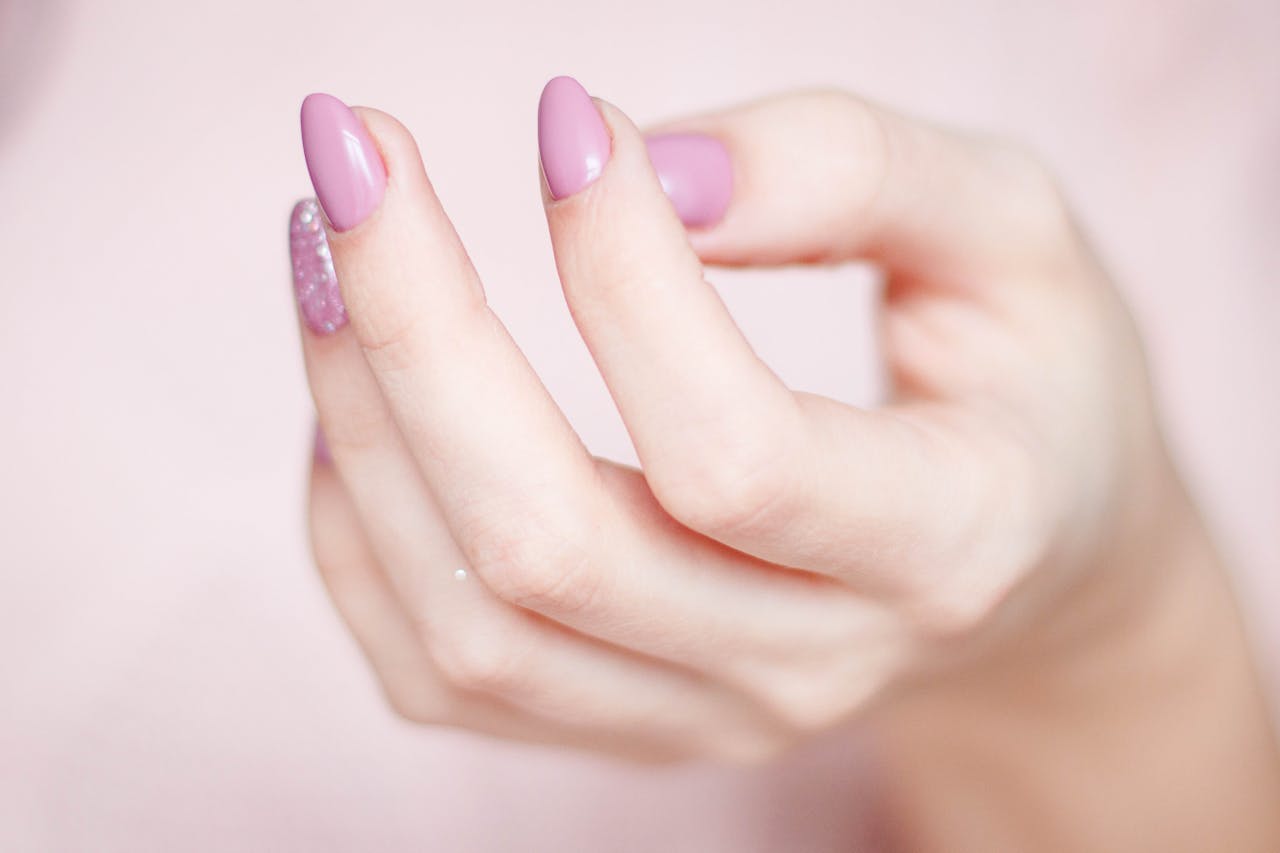 our-services-02 A close-up of a womans hand showing a stylish pink and glittery manicure.